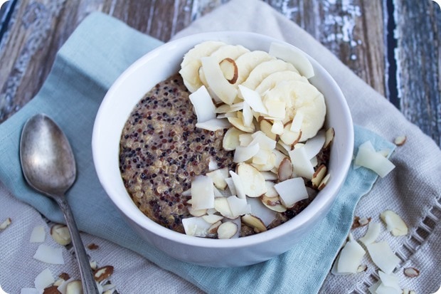 breakfast quinoa in a white bowl with coconut flakes, sliced almonds, and banana slices