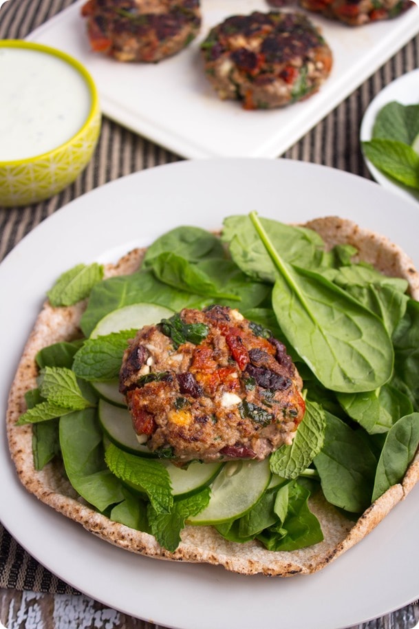 greek lamb burgers 3 a lamb burger patty sitting on a bed of spinach and cucumbers