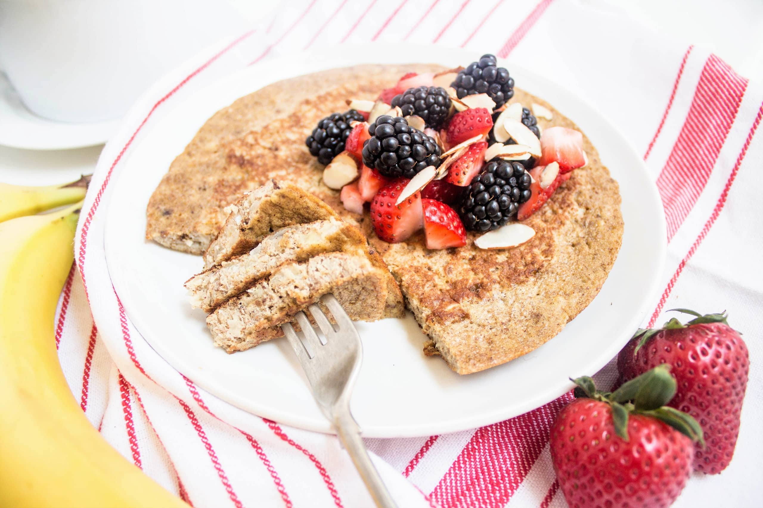 a banana pancake topped with berries and sliced almonds on a white plate