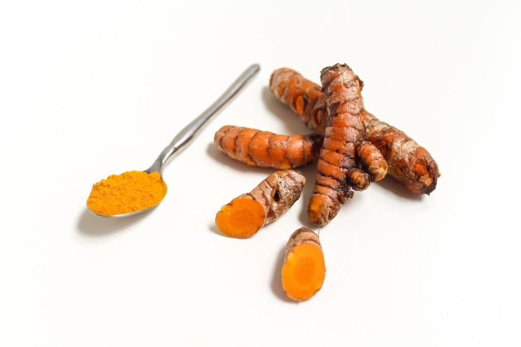 ground turmeric in a spoon next to fresh turmeric root