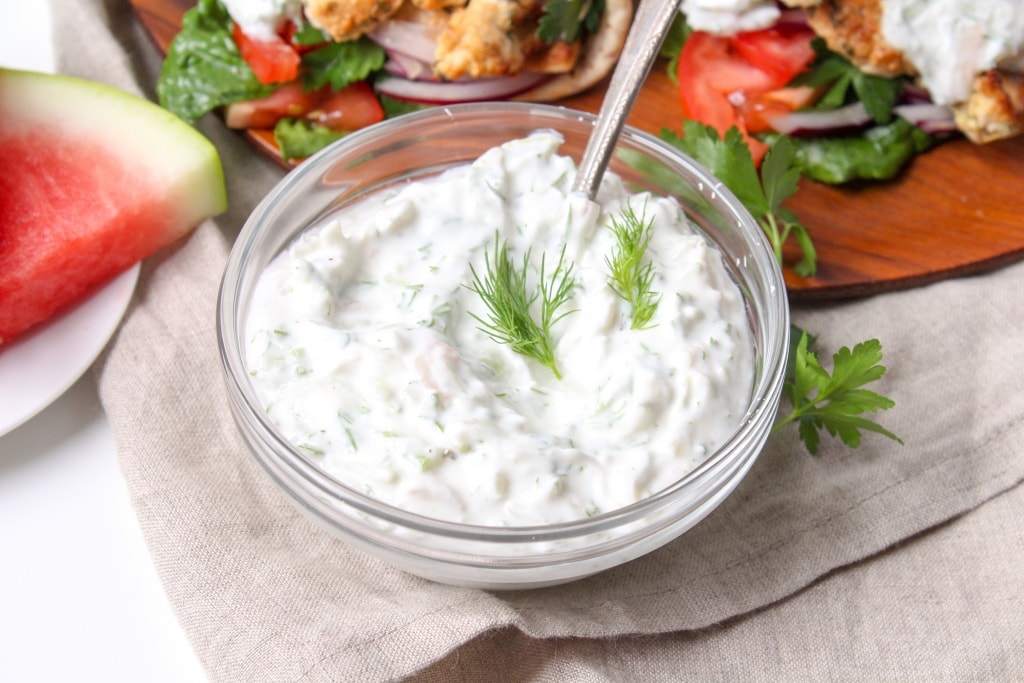 a small glass bowl with watermelon rind tzatziki sauce sitting on a beige linen napkin