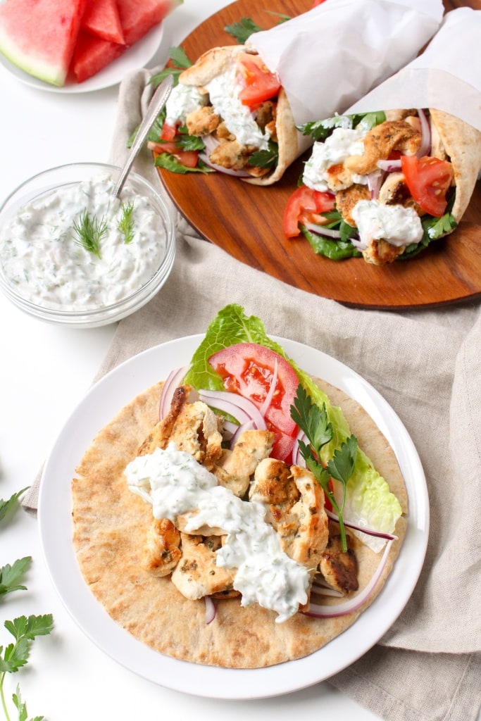 grilled chicken pita wraps with tomatoes, lettuce, and tzatziki sauce on a wooden platter