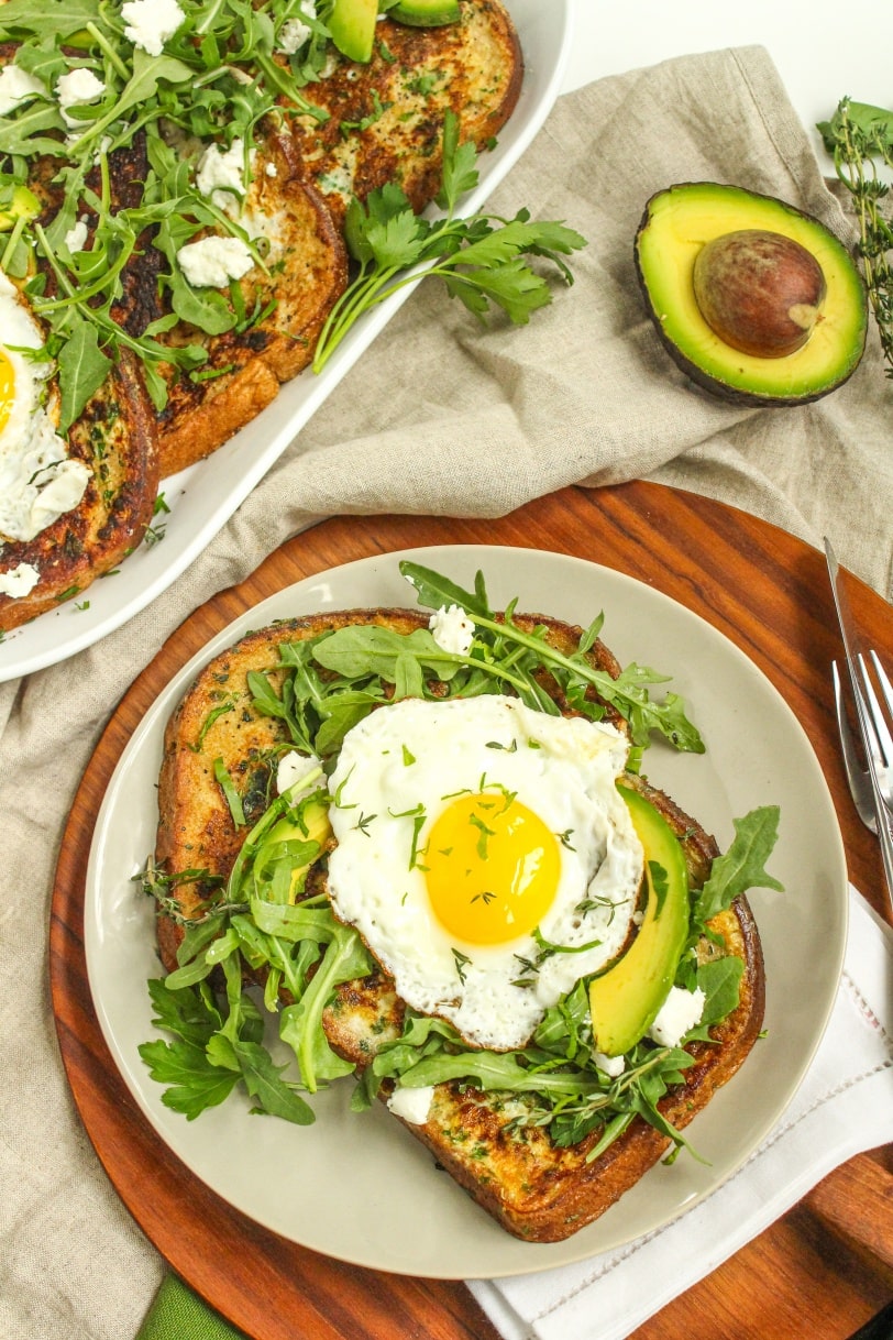 french toast with arugula, avocado, and fried eggs on top