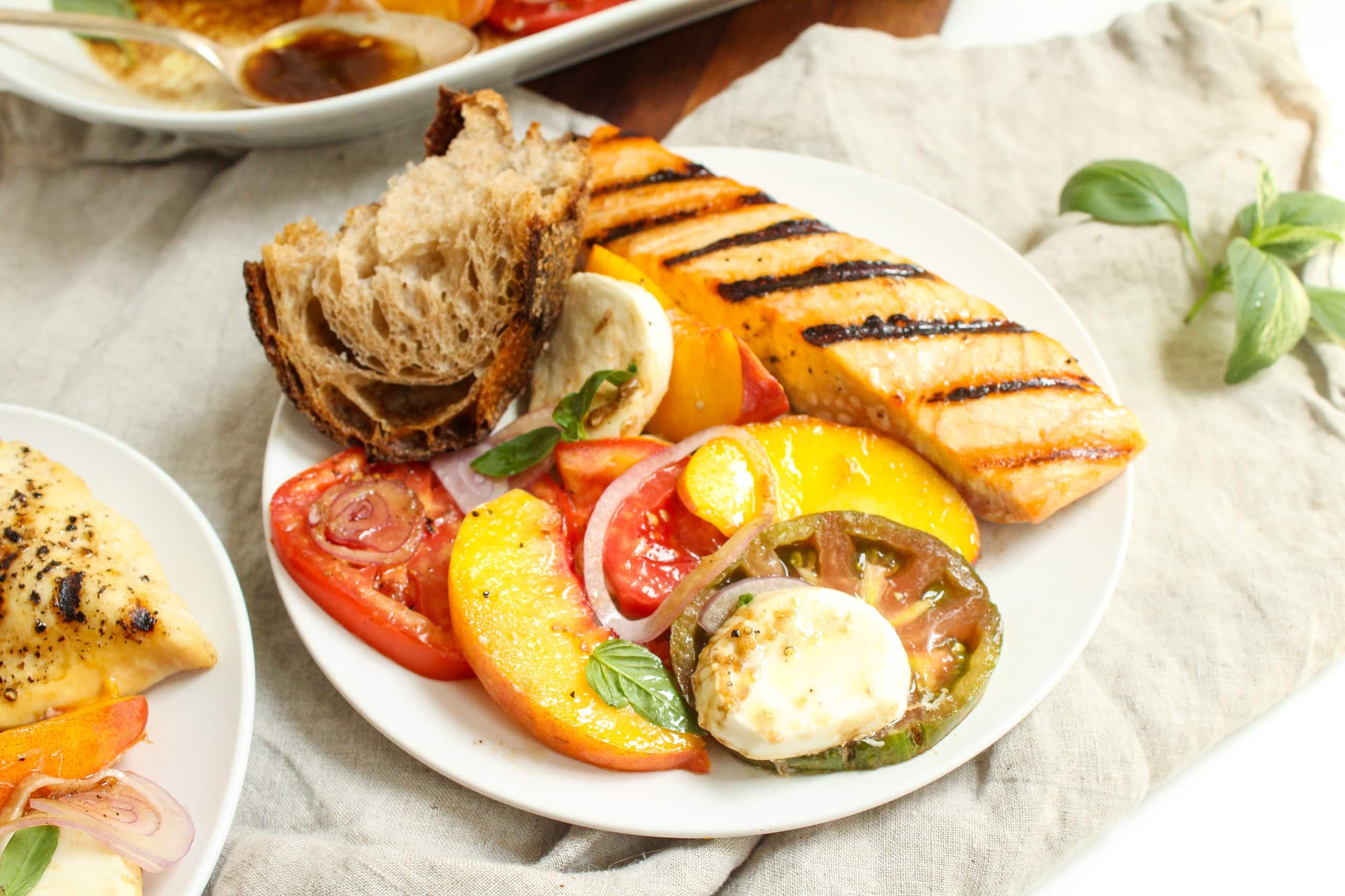 heirloom tomato peach caprese salad with grilled salmon and bread on a plate