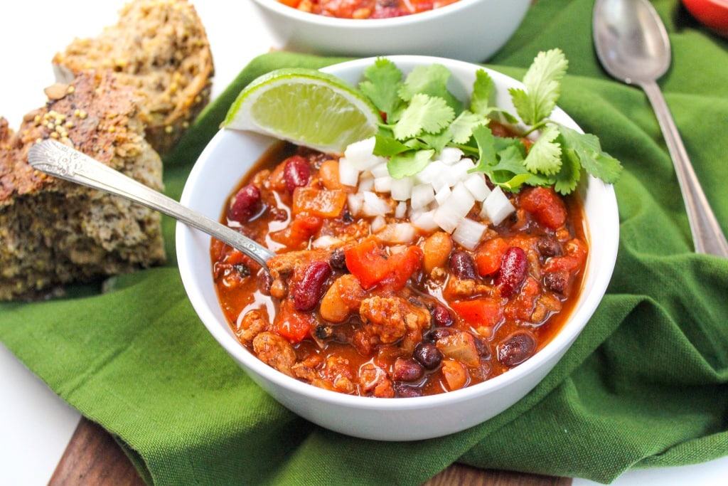 healthy slow cooker turkey chili in a white bowl with a lime, onions, and cilantro