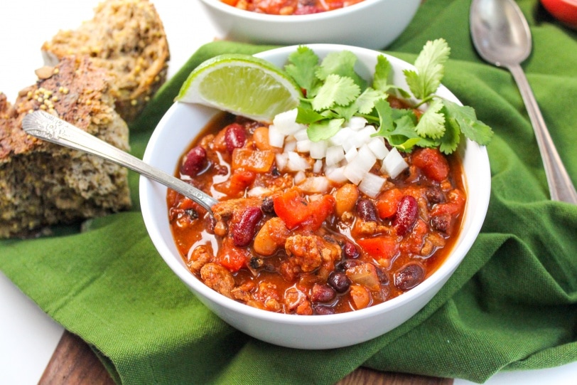 healthy slow cooker turkey chili in a white bowl with a lime, onions, and cilantro