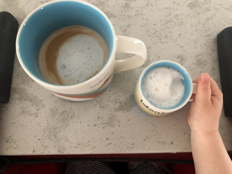 a large coffee cup holding a latte and a small espresso cup holding frothed milk