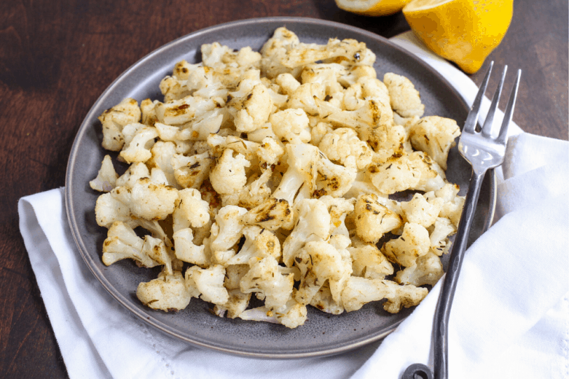 roasted cauliflower on a white plate with lemons