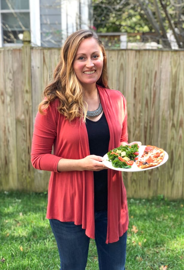 holding a plate of pizza and kale salad
