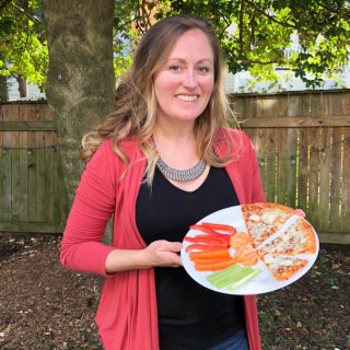 holding a plate with CPK cheese pizza, veggies, and fruit