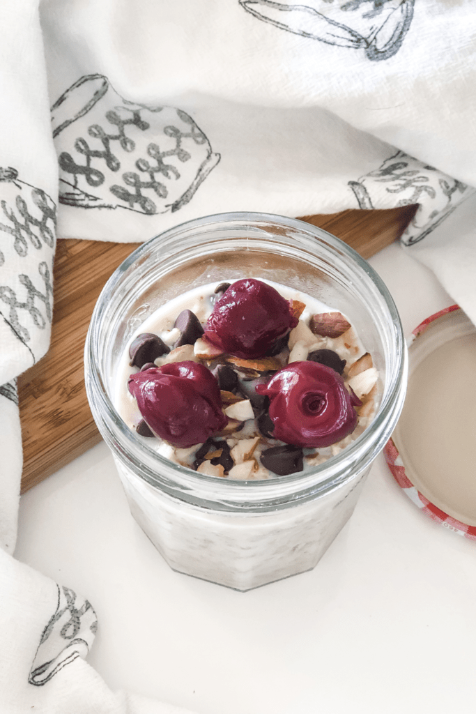 overnight oats with cherries, chocolate chips, and sliced almonds in a mason jar with a kitchen towel surrounding it