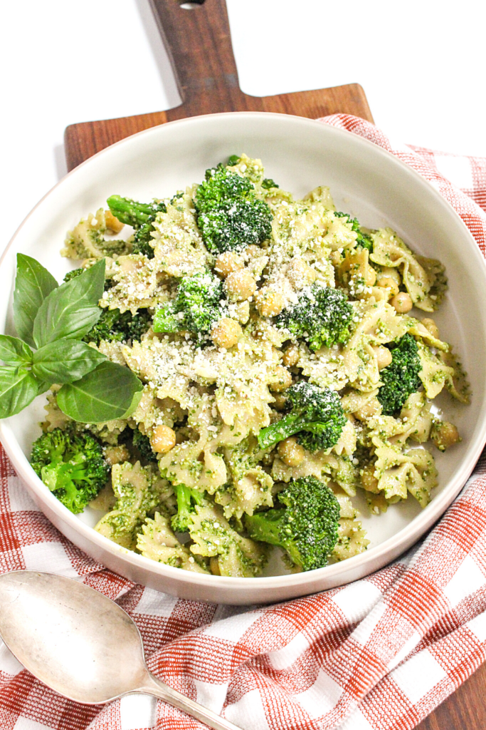 pesto pasta with broccoli and chickpeas in a white bowl on a checkered towel