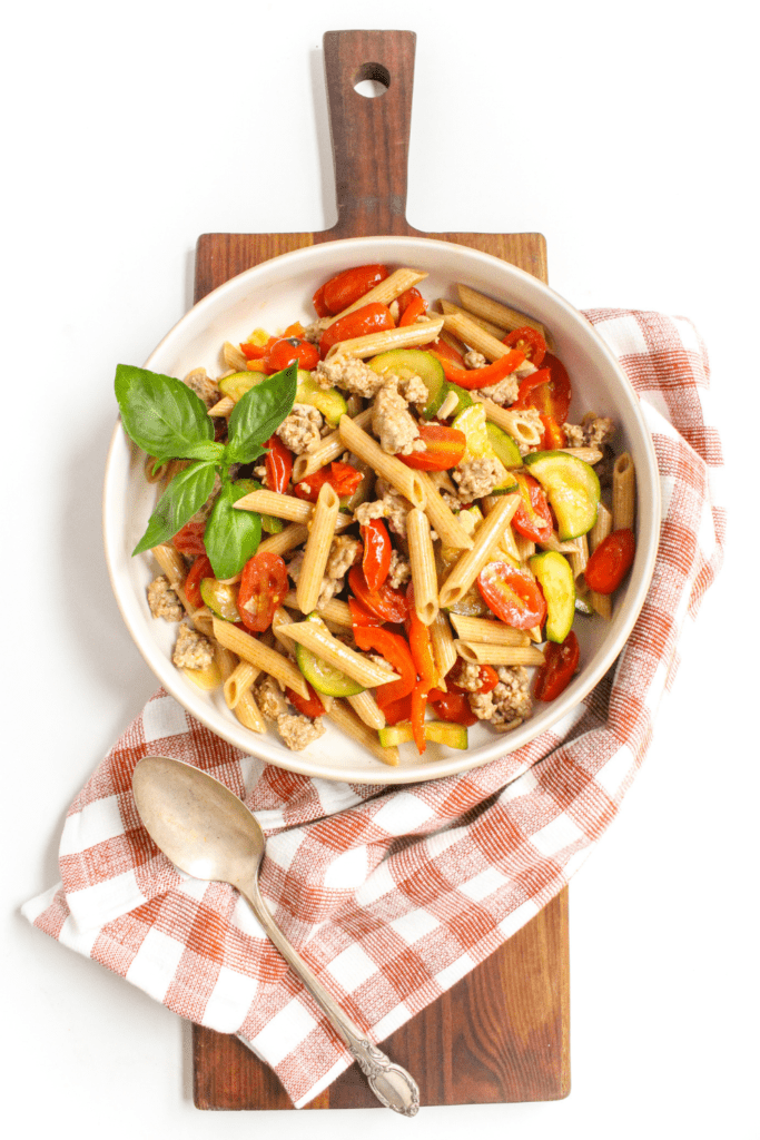 tomato garlic pasta in a white bowl on top of a wooden platter and checkered kitchen towel