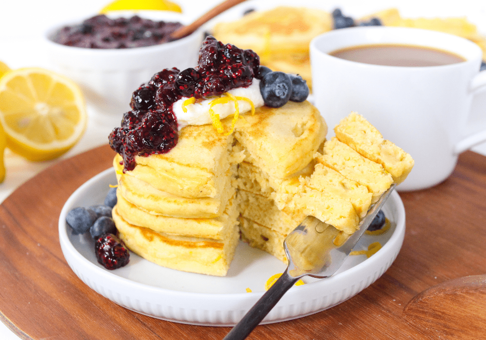 stack of lemon ricotta pancakes with blueberry jam topping and a white coffee mug in the background