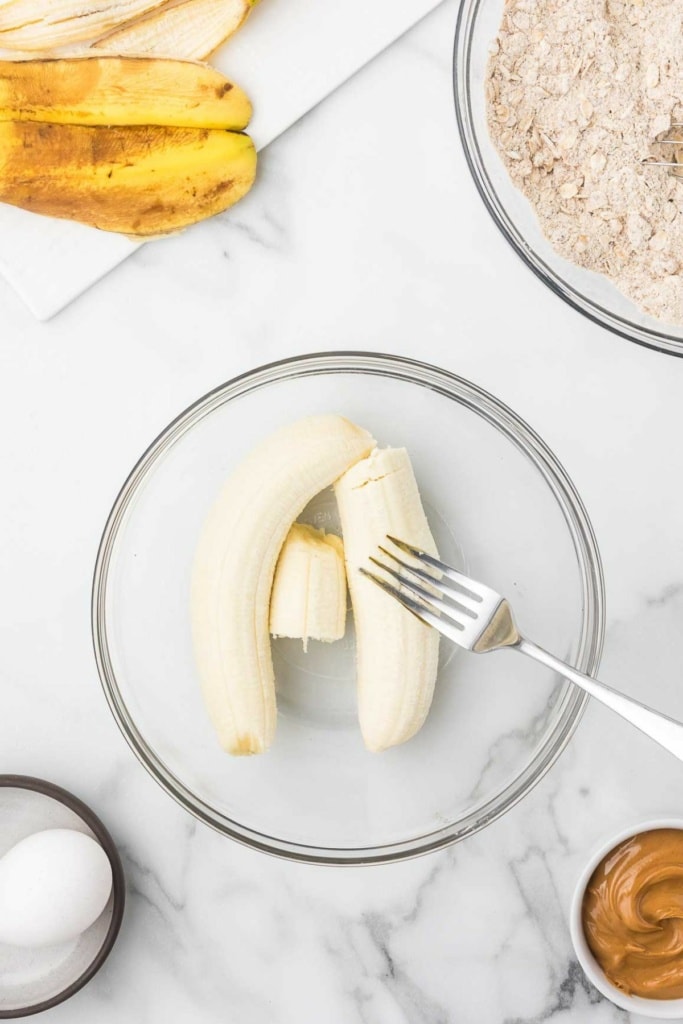 bananas being mashed with a fork in a glass bowl
