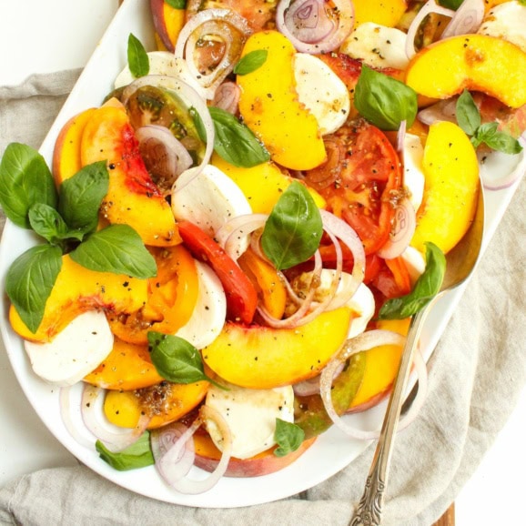 peach caprese salad with heirloom tomatoes and fresh mozzarella on a white platter