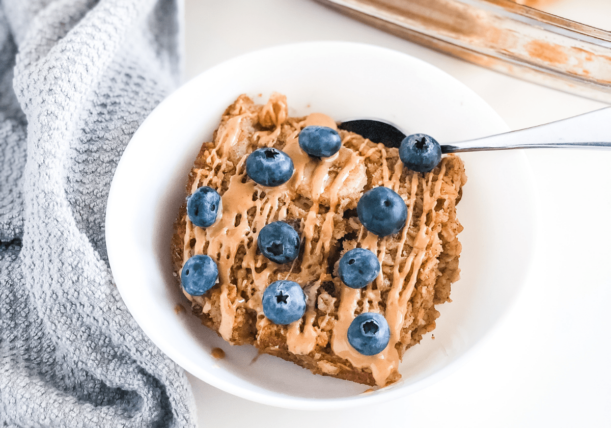 blueberry banana baked oatmeal in a white bowl next to a grey kitchen towel