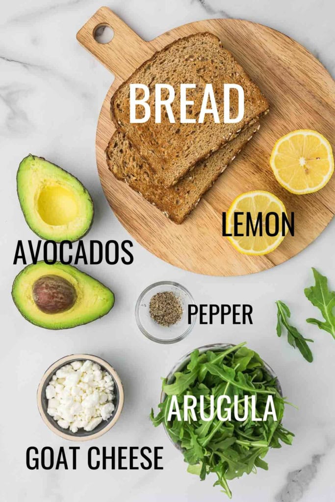 bread, avocados, goat cheese, arugula, and lemons on a white marble countertop
