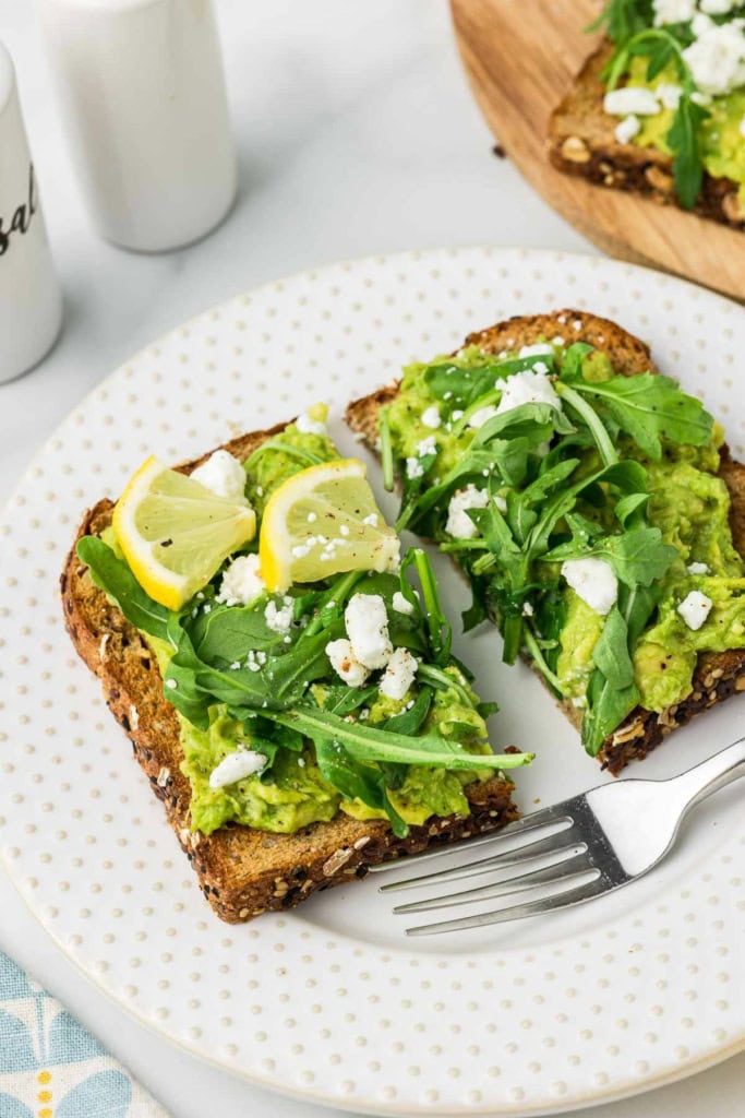 avocado toast with arugula and lemon on a white plate