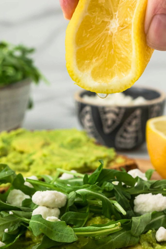 lemon being squeezed over arugula and goat cheese