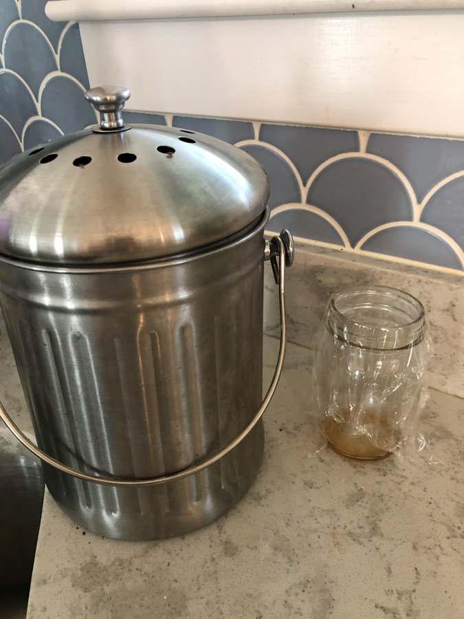 compost bin on a countertop with a jar of vinegar next to it.