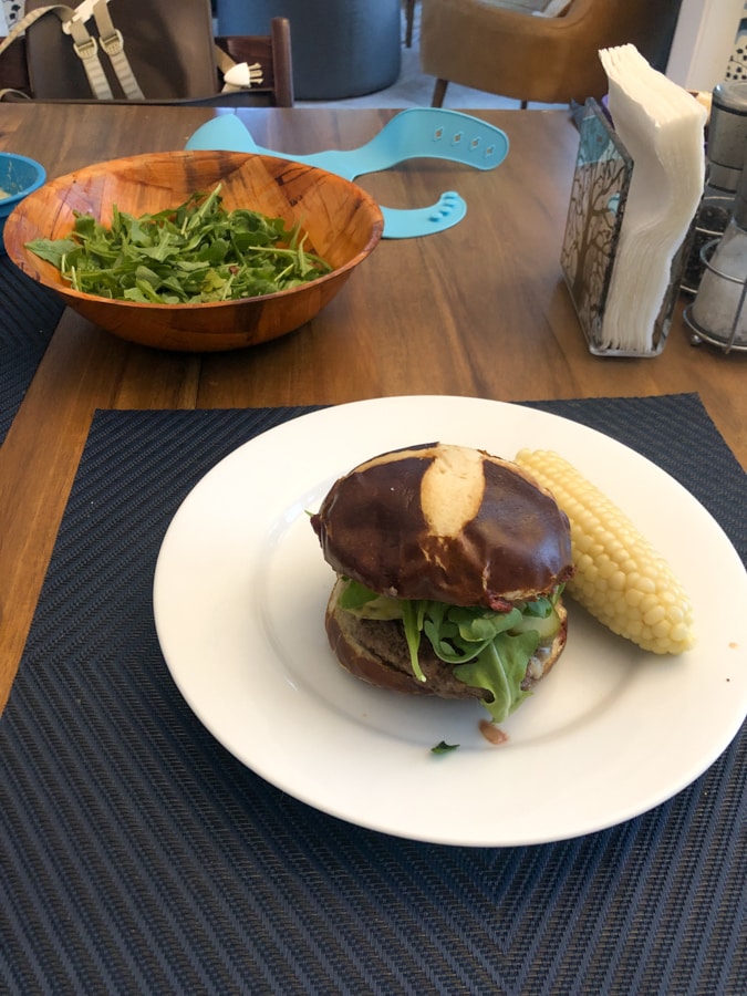 burger with a pretzel bun plus salad and corn.