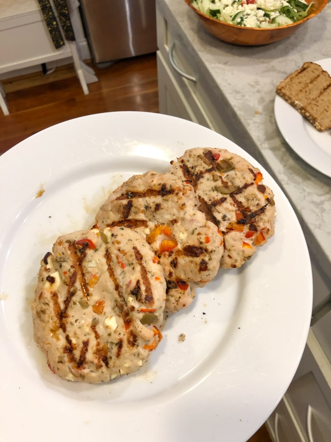 turkey burgers with olives, red pepper, and feta on a white plate.
