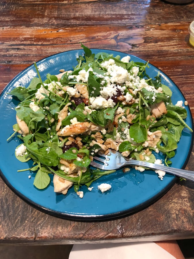 arugula salad with chicken, dried cherries, feta, farro on a blue plate.