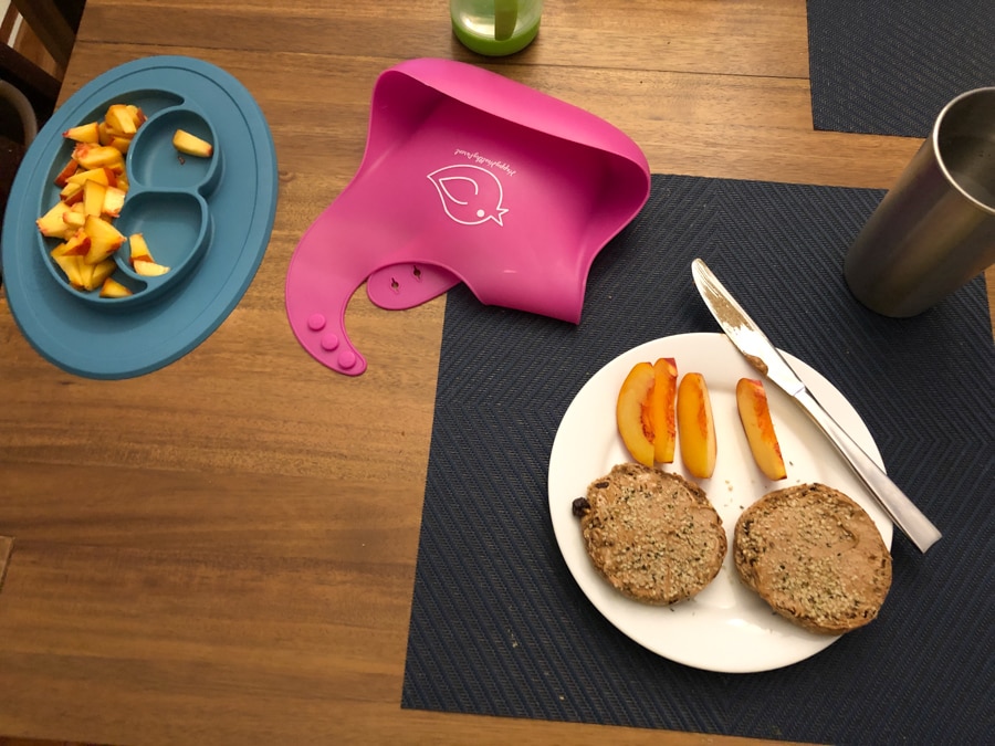 english muffin with almond butter and a sliced peach on a white plate.