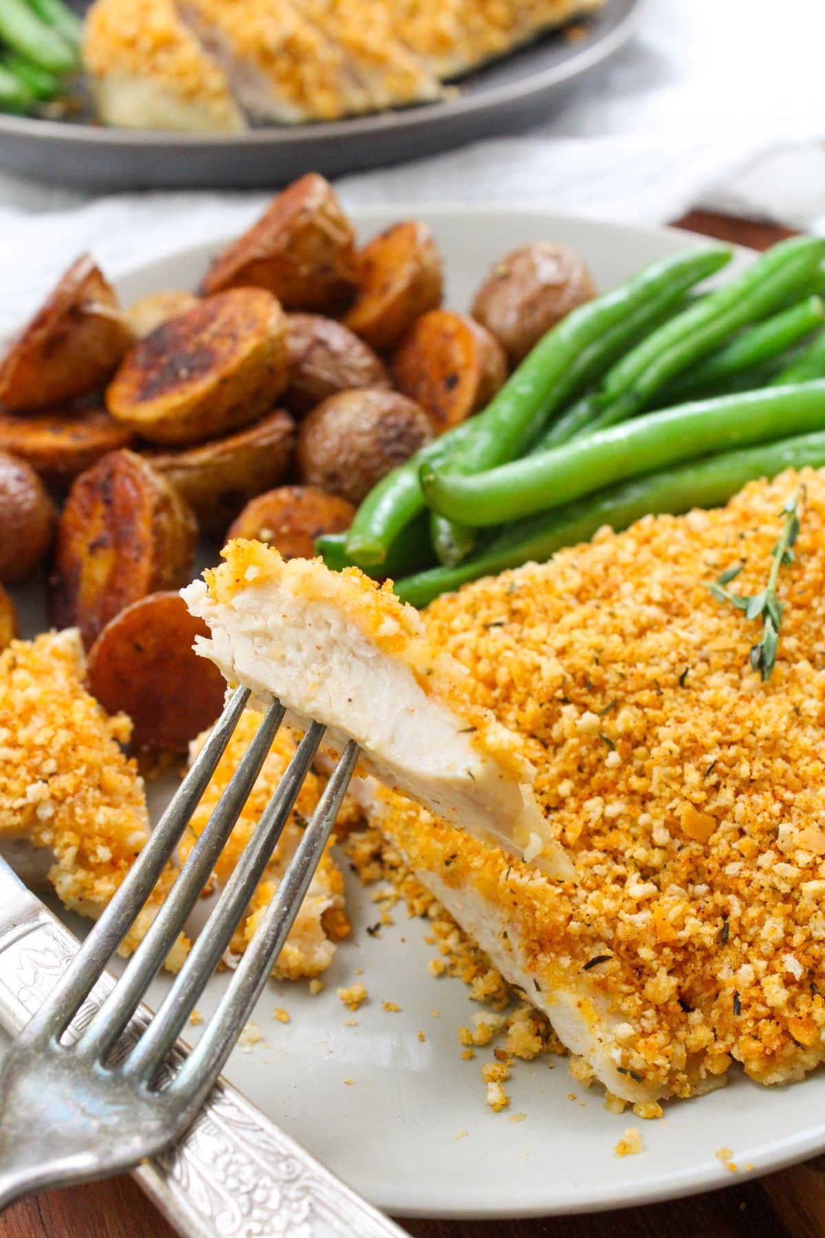 a bit of panko chicken on a fork with roasted mini potatoes and green beans