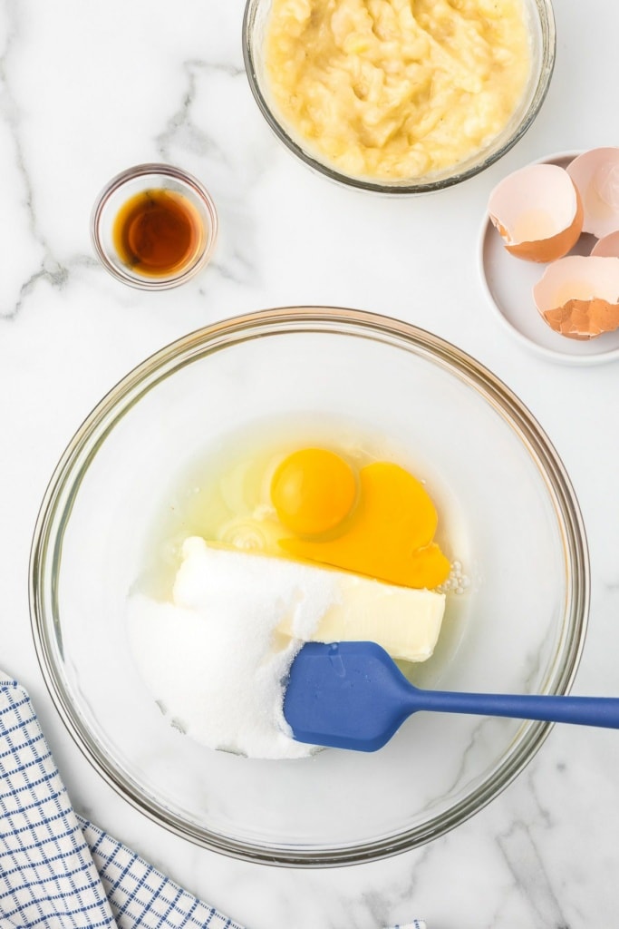 eggs, sugar, and softened butter in a bowl next to mashed bananas