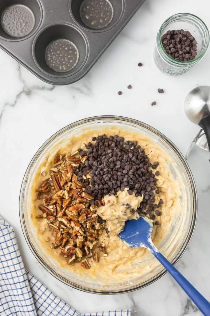 muffin batter in a glass bowl with chopped pecans and mini chocolate chips