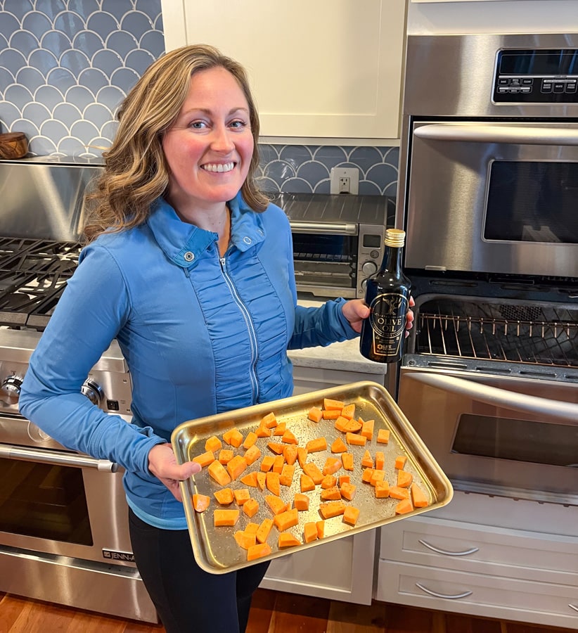 anne mauney holding a sheet pan of sweet potatoes and a bottle of olive oil
