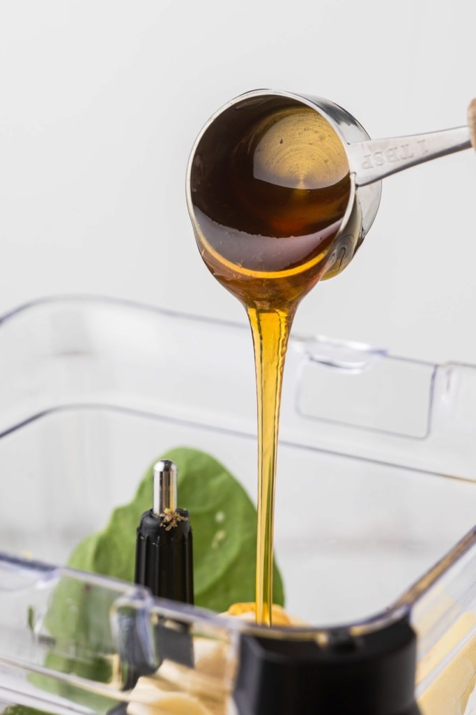 honey in a measuring cup being poured into a blender