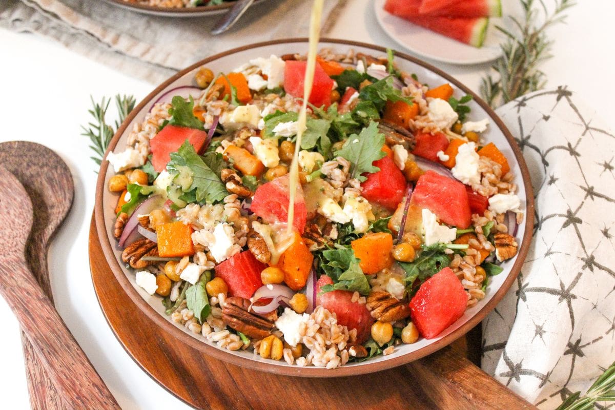 harvest watermelon salad in a shallow bowl with dressing being poured over it